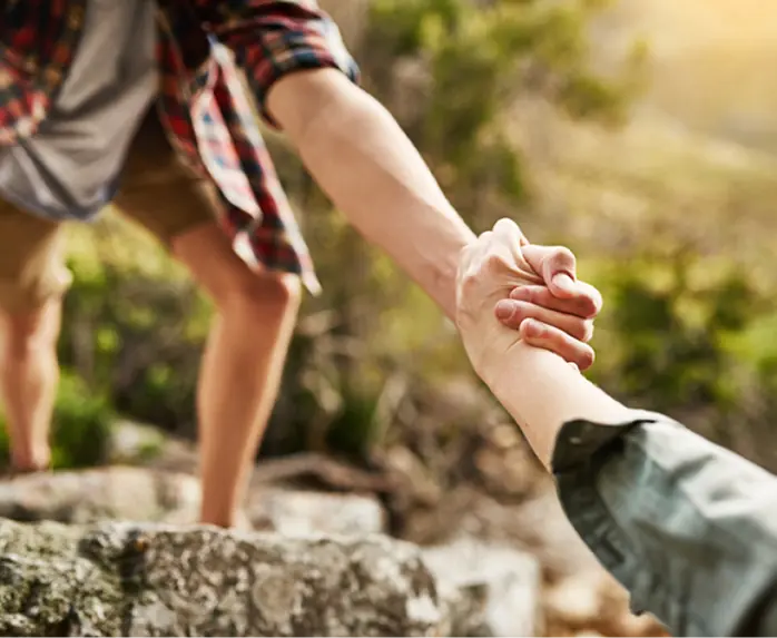 Eine Hand unterstützt einen anderen Menschen beim Aufstieg als Symbol für Begleitung und Unterstützung in herausfordernden Lebensphasen.